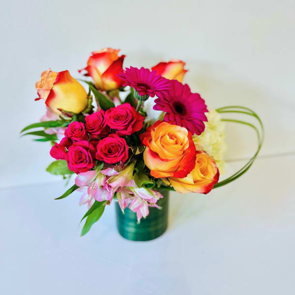 Bouquet of pink and orange roses with magenta daisies in a green vase