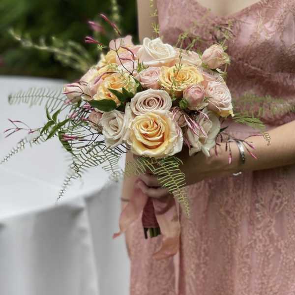 Handheld bouquet of blush and cream roses with airy greenery