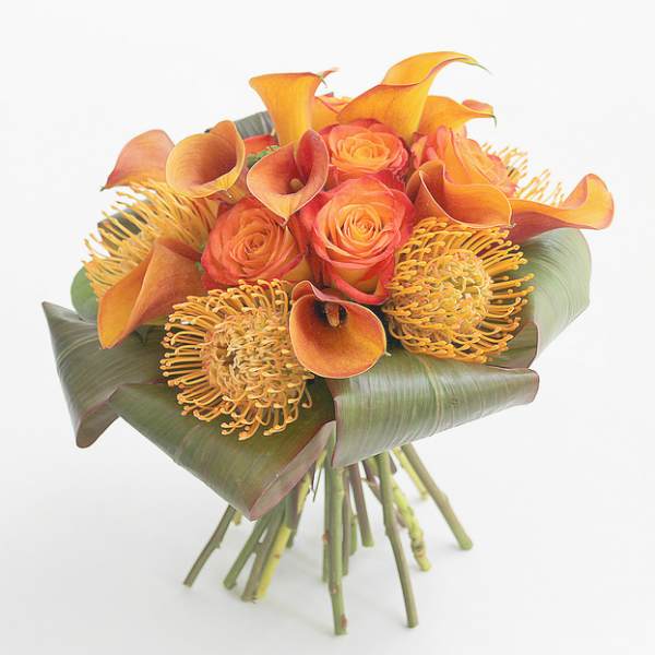 Orange roses and calla lilies with yellow pincushion blooms in a hand-tied bouquet