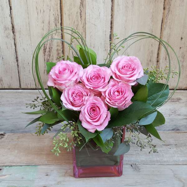 Pink roses arranged in a square glass vase with looping wire accents