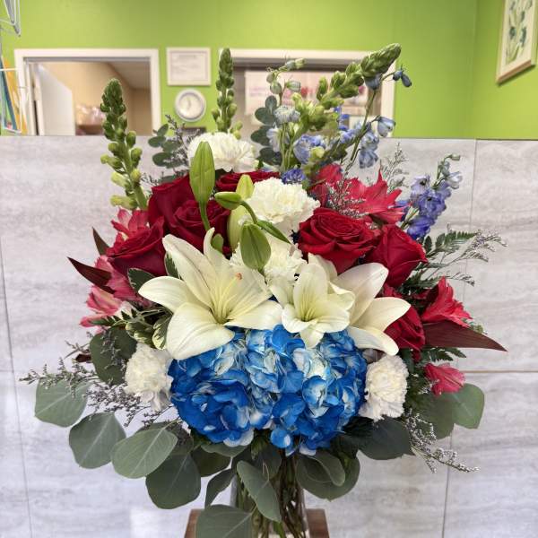 Bouquet of red roses, white lilies, and blue hydrangeas in a glass vase