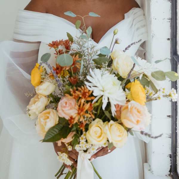 Bride holding a bouquet of cream, yellow, and orange flowers