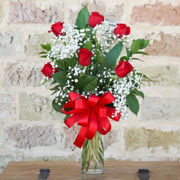Bouquet of red roses with white baby's breath and a red ribbon in a glass vase