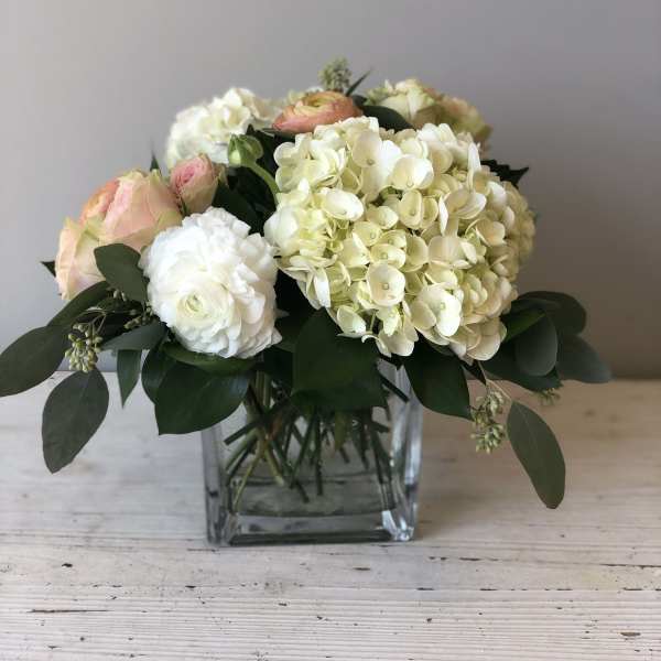 Low arrangement of white hydrangeas and pale roses in a clear glass cube vase