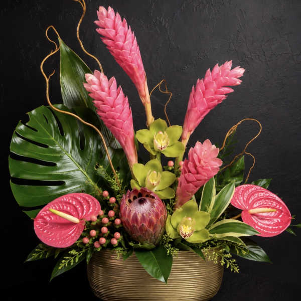 Tropical arrangement with pink blooms and green orchids in a gold vase