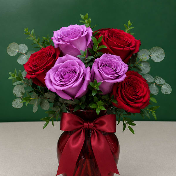 Bouquet of red and lavender roses in a red glass vase with a ribbon