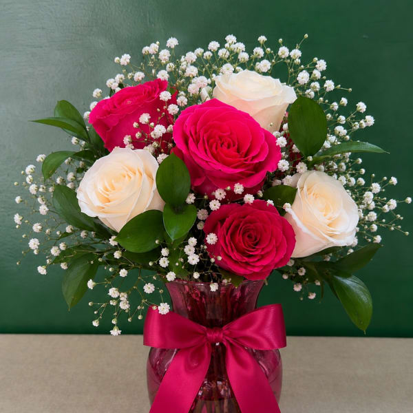 Pink and white roses in a magenta vase with a ribbon bow