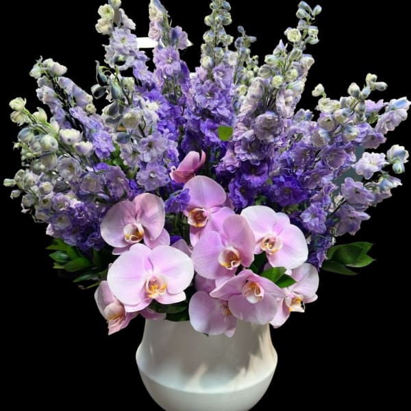 Pink orchids and purple flowers arranged in a white vase
