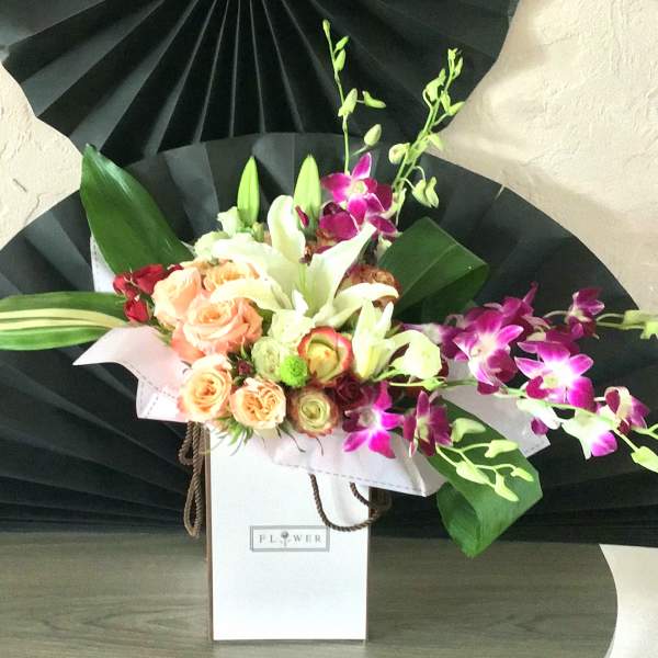 Bouquet of peach roses, white lilies, and purple orchids in a white gift box