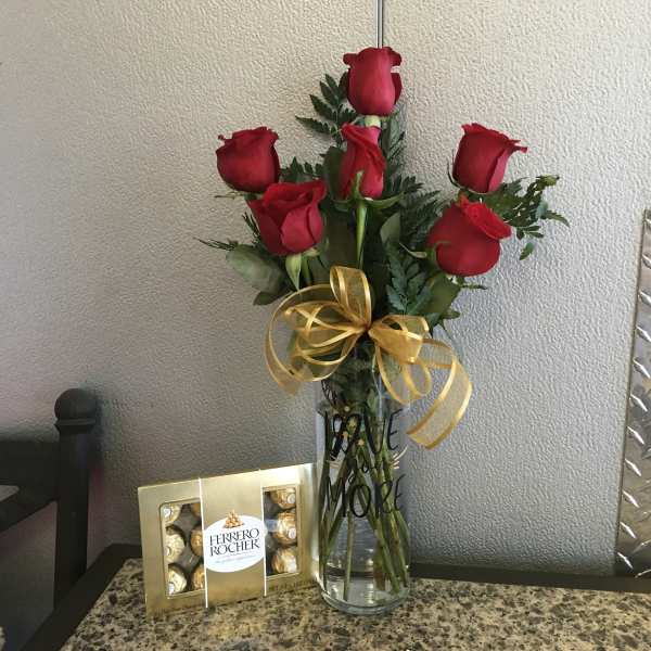 Red roses in a clear vase with a gold ribbon and chocolate box beside it