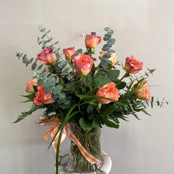 Pink-orange roses in a clear glass vase with eucalyptus and a ribbon