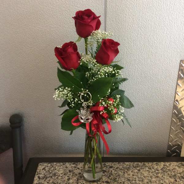 Three red roses in a clear glass vase with a red ribbon and charm