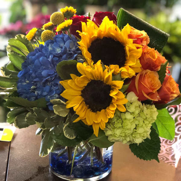 Bouquet with sunflowers, blue hydrangea, and orange roses in a glass vase