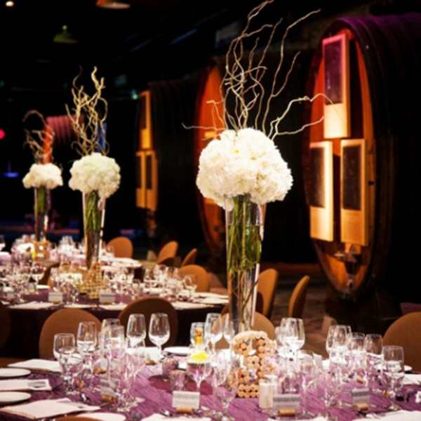 Tall white floral centerpieces on banquet tables in a dim event hall