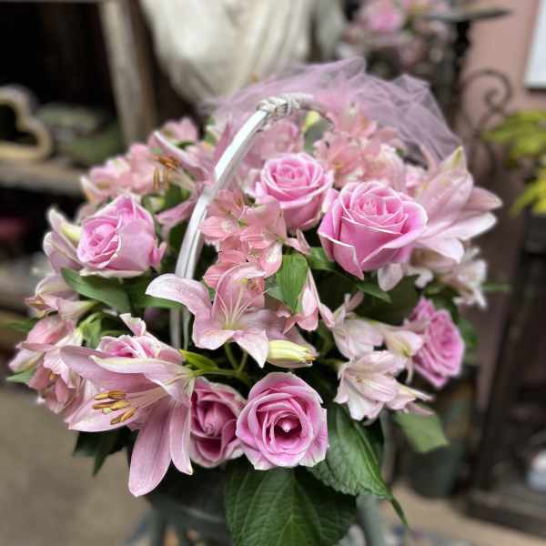 Pink roses and lilies arranged in a basket with a tulle bow
