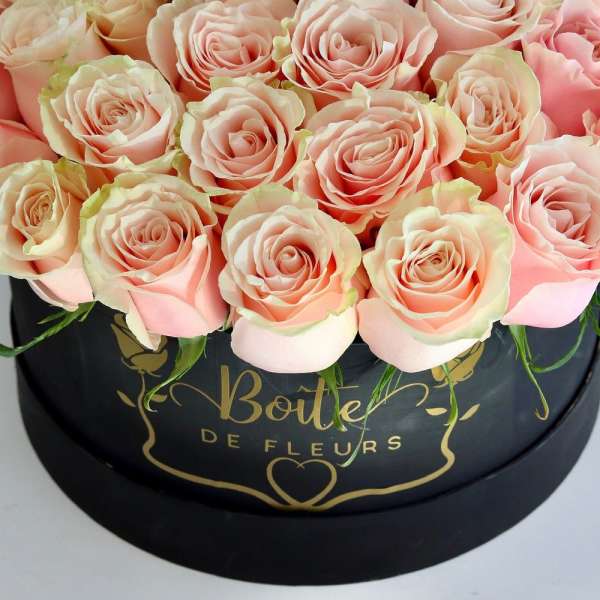 Pink roses arranged in a black round box with gold lettering