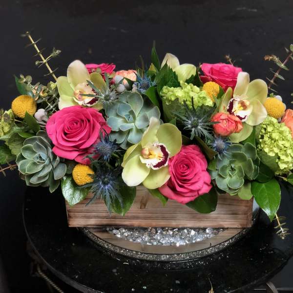 Pink roses and pale orchids in a wooden box with succulents