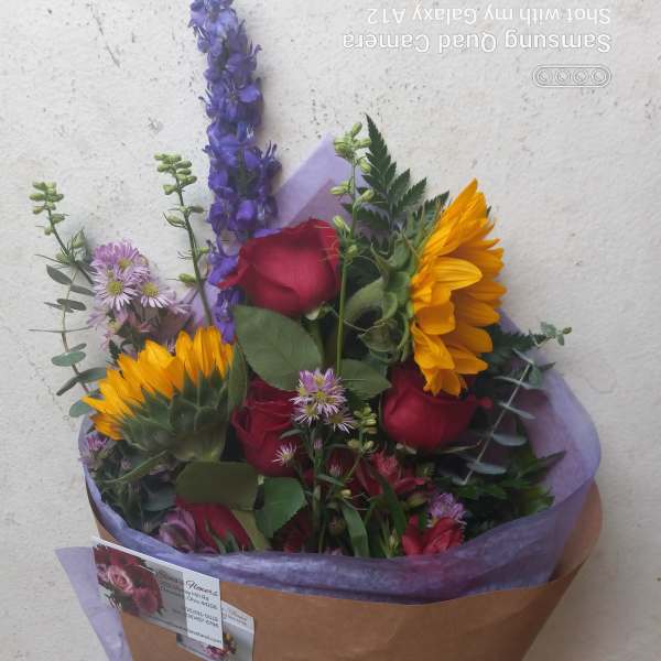 Bouquet of red roses, sunflowers, and purple flowers wrapped in brown paper