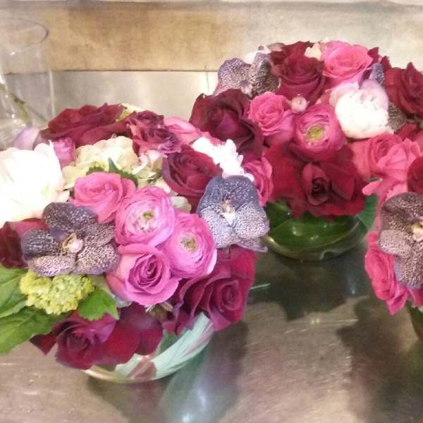 Three pink and burgundy rose arrangements in glass bowls