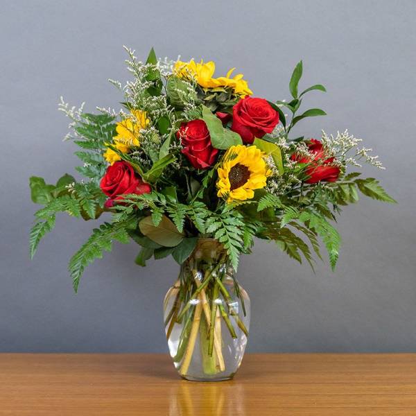 Bouquet of red roses and yellow sunflowers in a clear glass vase