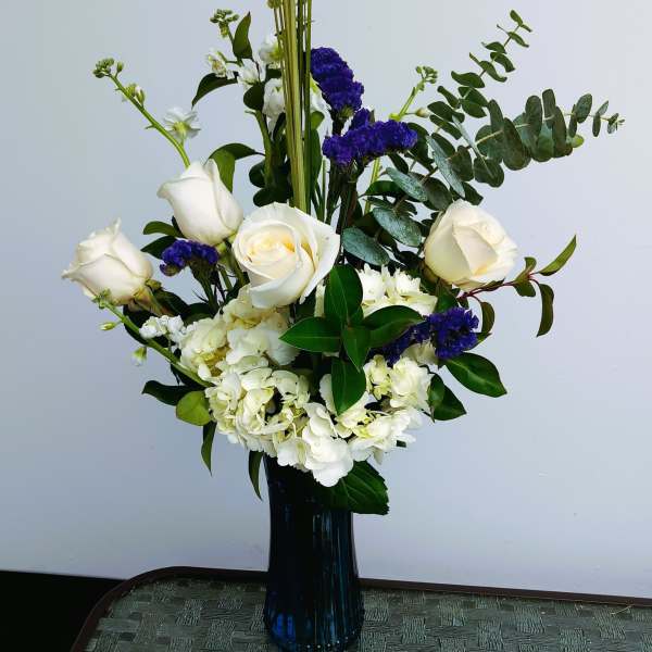 White roses and hydrangeas in a tall blue vase with purple accents