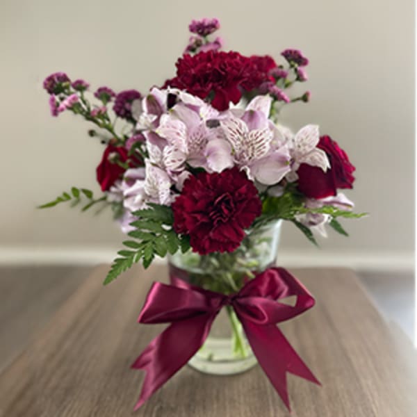 Bouquet of burgundy and pale pink flowers in a glass vase with a ribbon