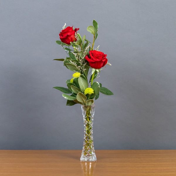 Two red roses in a clear glass vase with greenery
