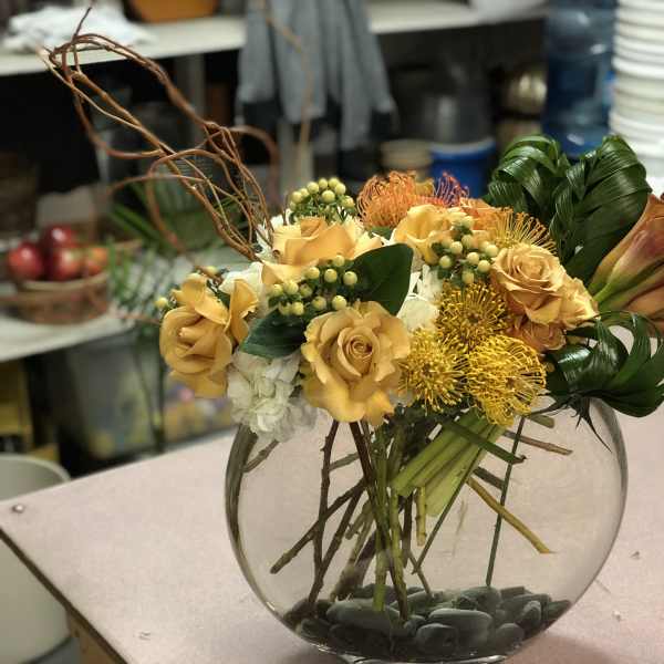 Yellow roses and orange flowers arranged in a round glass vase