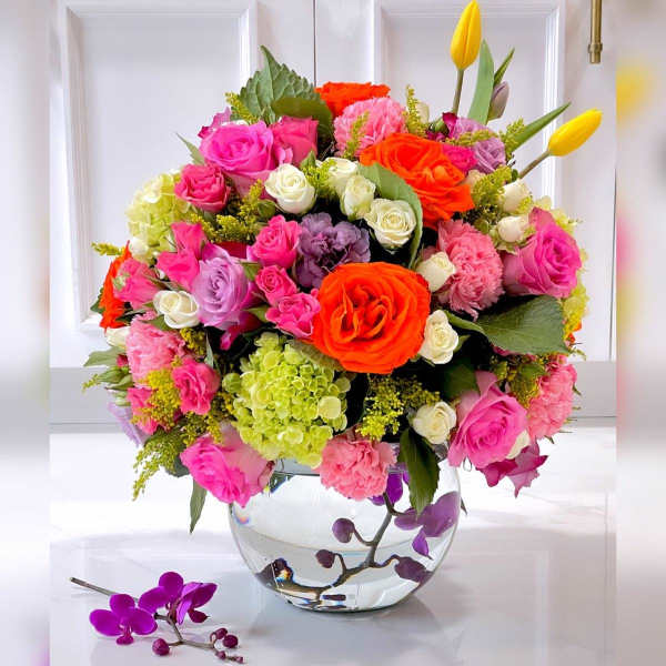 Bright mixed bouquet of roses, tulips, hydrangea, and carnations in a clear glass vase