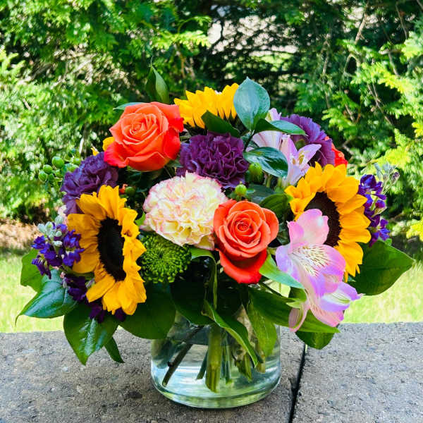 Colorful bouquet with sunflowers, roses, carnations, and alstroemeria in a glass vase