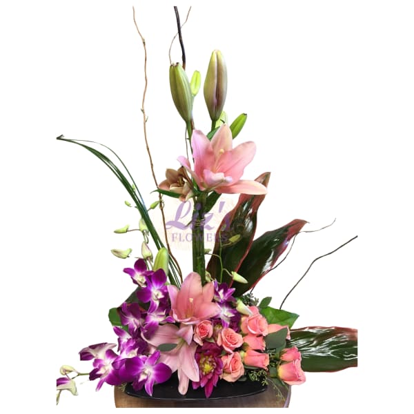 Tall floral arrangement with pink lilies, purple orchids, and roses in a low container