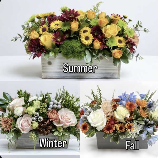 Three seasonal floral arrangements in wooden boxes labeled summer, winter, and fall.