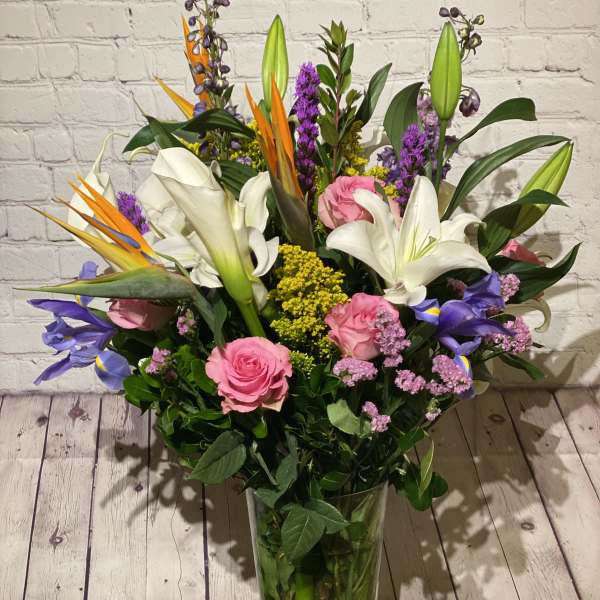Tall mixed bouquet with white lilies, pink roses, and purple flowers in a glass vase