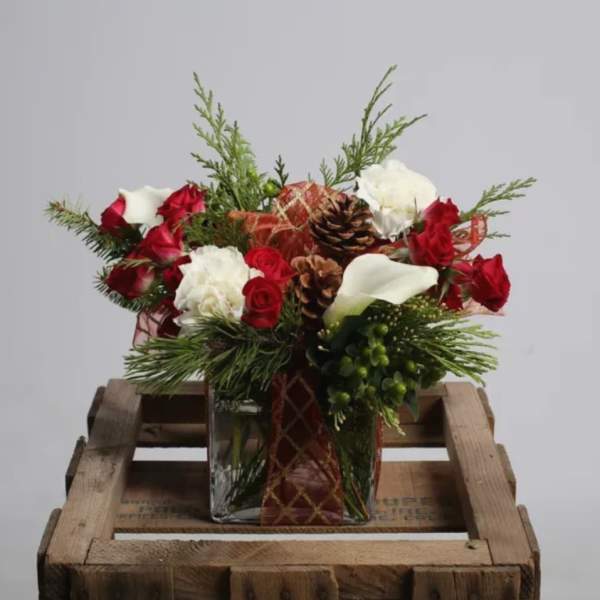 Red and white floral arrangement in a square glass vase with pinecones