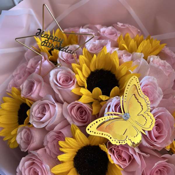 Bouquet of pink roses and yellow sunflowers with a birthday topper and butterfly decoration