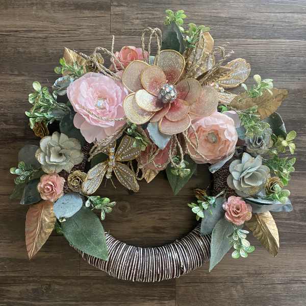 Decorative floral wreath with pink and gold flowers on a wrapped ring base
