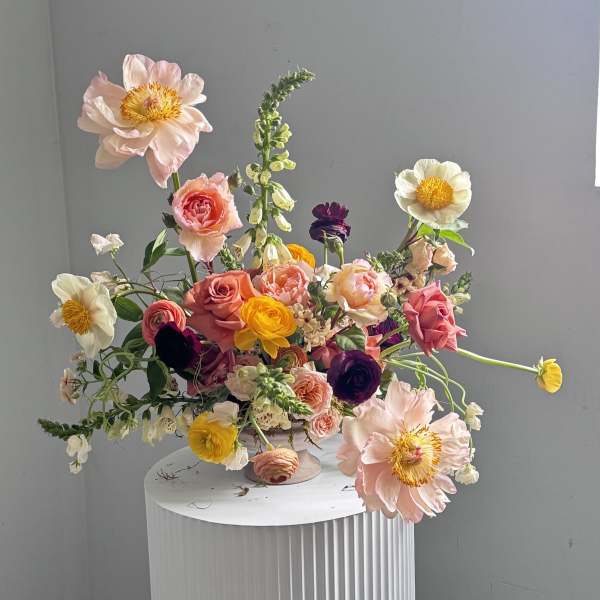 Mixed bouquet of pink, yellow, white, and purple flowers in a pedestal vase