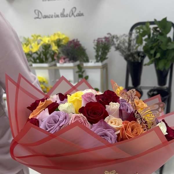 Bouquet of multicolored roses wrapped in pink paper with a red ribbon