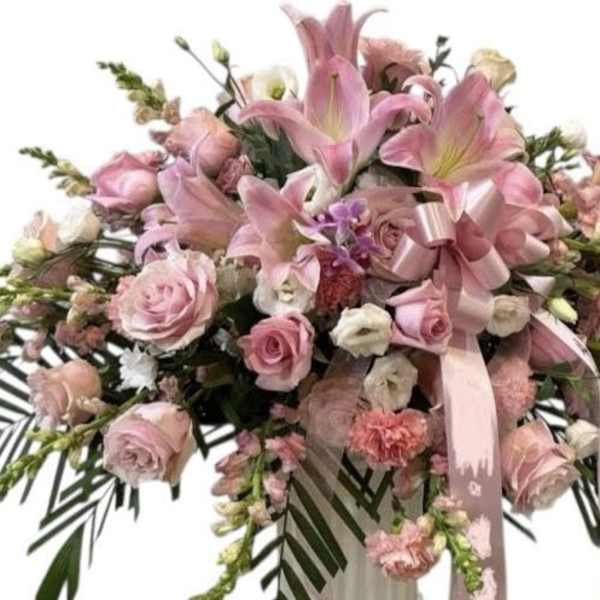 Pink floral spray with roses and lilies, accented by a pink ribbon