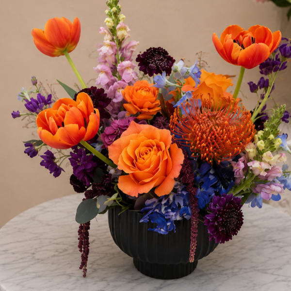 Bright mixed bouquet in a black vase with orange, purple, and blue flowers