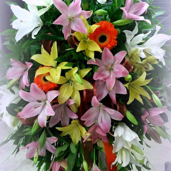 Tall standing spray of lilies and gerbera daisies in pink, white, and yellow