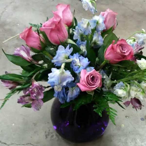 Pink roses and blue flowers arranged in a dark glass vase