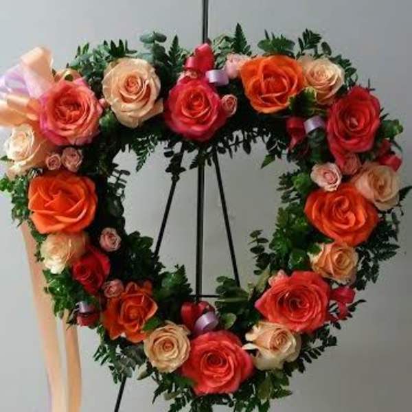 Heart-shaped rose wreath on an easel with peach and red blooms