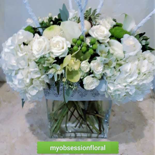White rose arrangement in a clear square vase with green accents