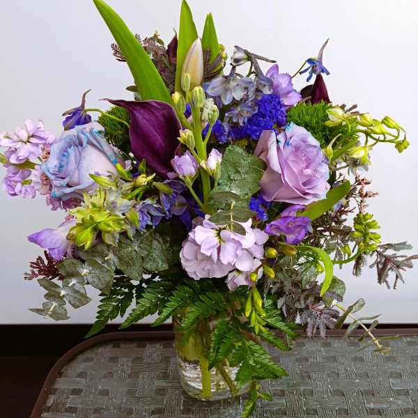 Mixed purple and lavender flowers arranged in a clear glass vase