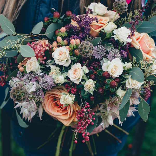 Bouquet of peach and white roses with purple accents and berries
