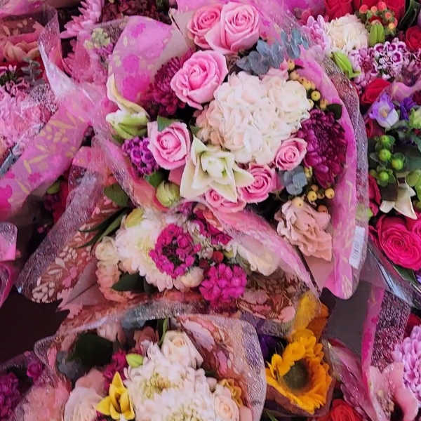 Assorted bouquets of pink, white, and red flowers wrapped in pink paper
