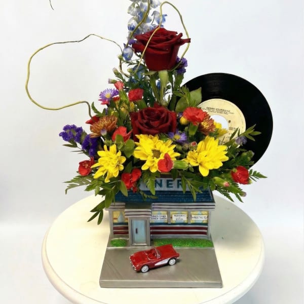 Mixed flower arrangement with roses, daisies, and a vinyl record on a decorative base