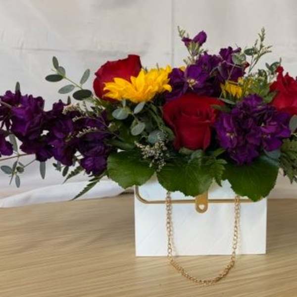 Mixed bouquet of red roses, purple flowers, and a yellow bloom in a white box