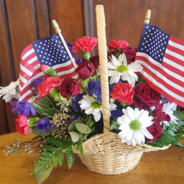 Basket arrangement of red roses, carnations, and white daisies with two American flags